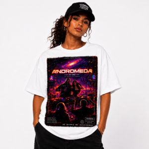 Woman modeling a white oversized T-shirt with a neon space-poster graphic reading 'ANDROMEDA' and a cosmic scene in red and purple hues, cap on head, hands in pockets.