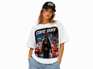 Woman modeling a white graphic T‑shirt with a neon cityscape design and the words 'STATIC SKIES' while wearing a black cap and jeans.
