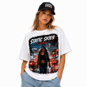 Woman modeling a white graphic T‑shirt with a neon cityscape design and the words 'STATIC SKIES' while wearing a black cap and jeans.