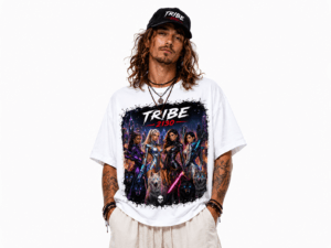 Model wearing a white graphic T‑shirt with a sci‑fi group of women and wolves and the text 'TRIBE 2130', cap on head, hands in pockets.